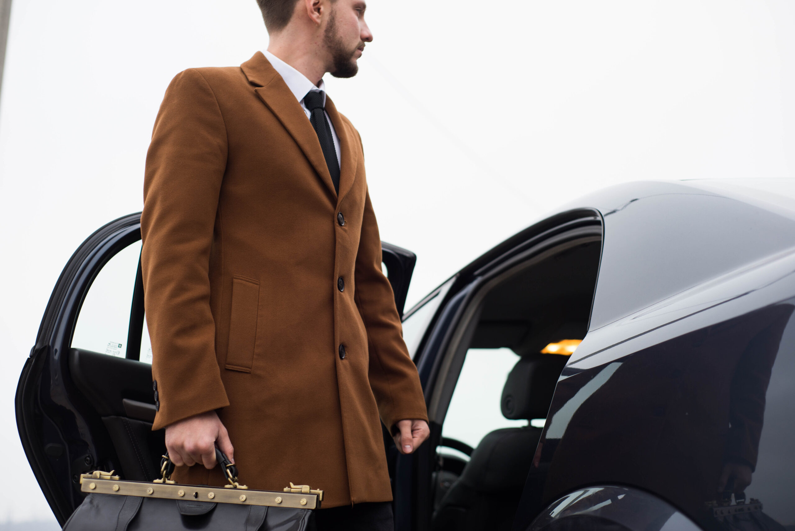 Man in coat exits car with briefcase