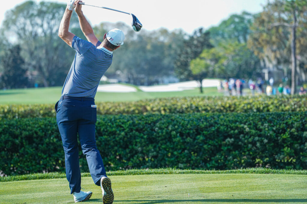 Golfer swinging club on a sunny golf course.