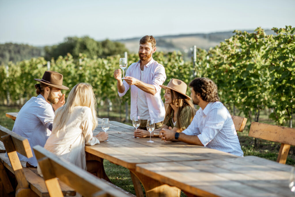 People wine tasting at vineyard table outdoors.